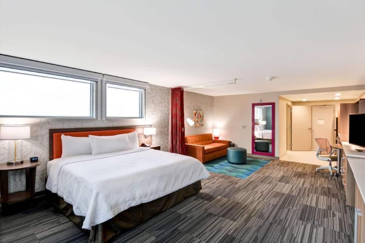 A hotel room with a bed, a desk, a chair, a TV, and a bathroom.