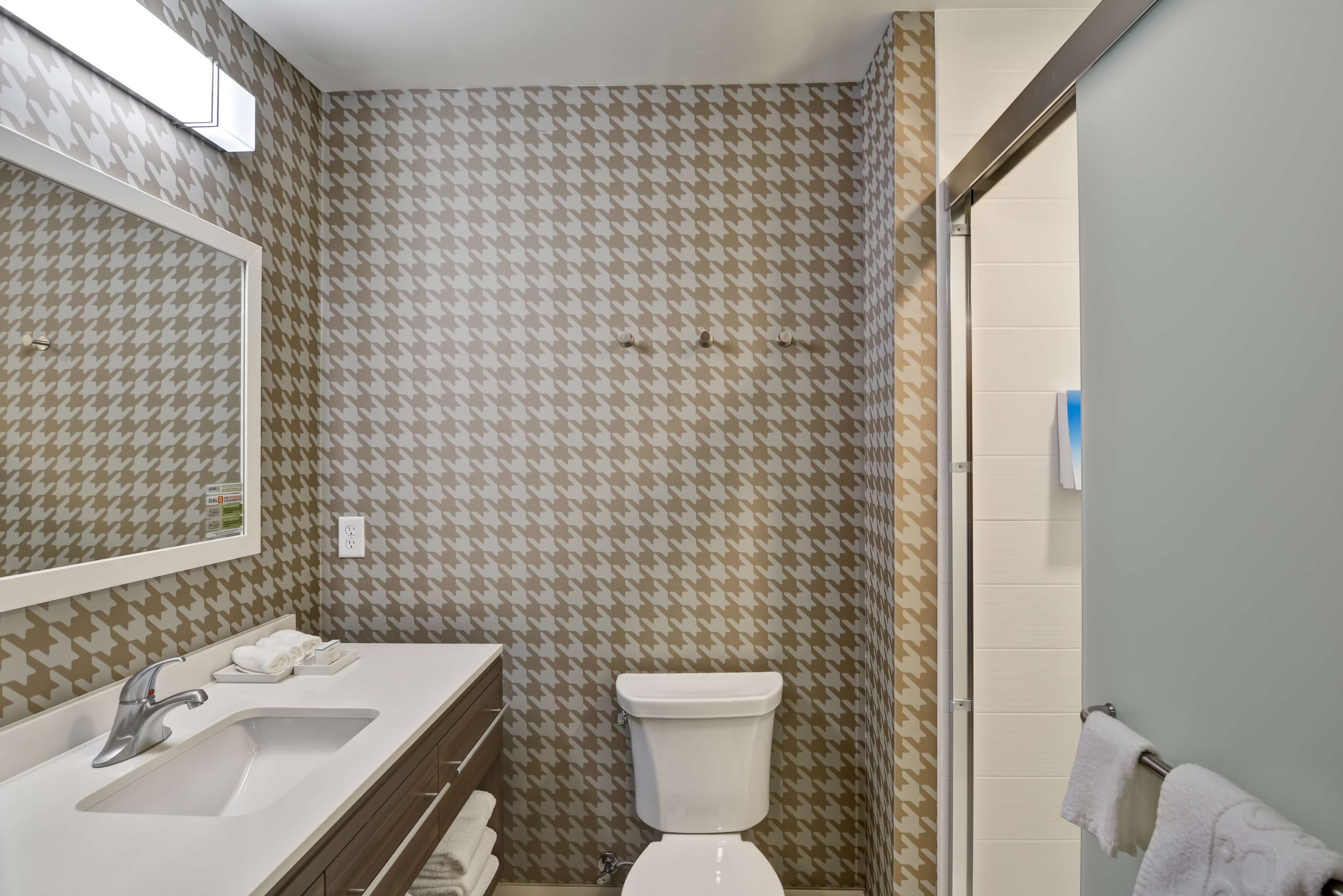 A bathroom with a houndstooth patterned wall, a white sink, a mirror, and a toilet.