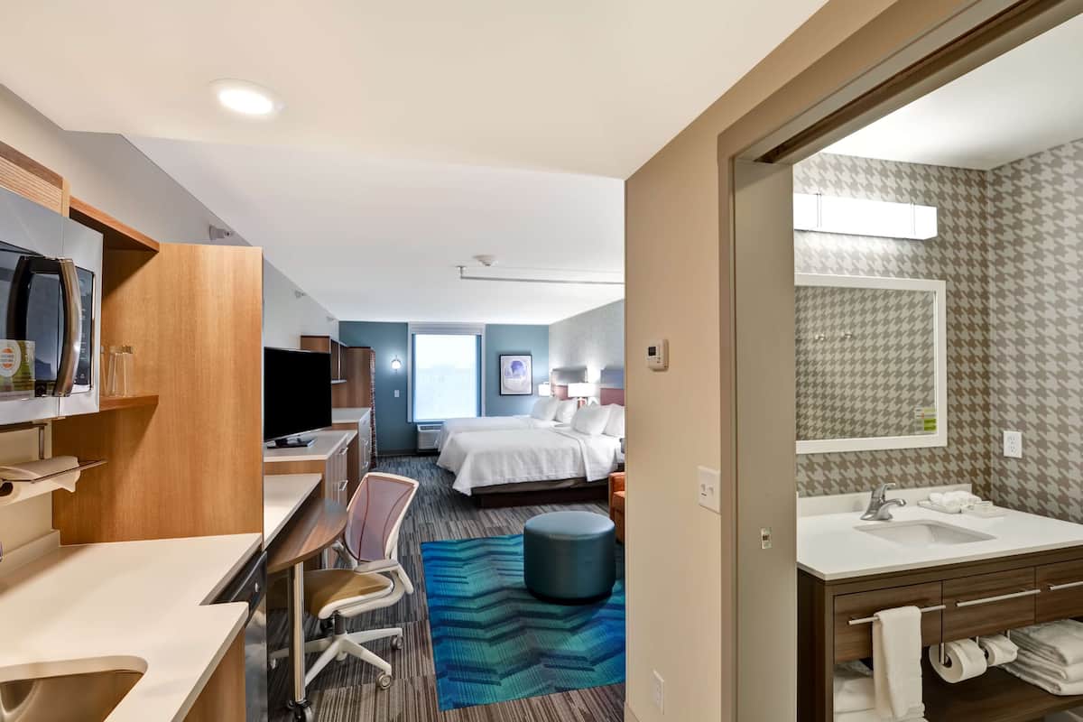 A hotel room with a bed, desk, chair, and a bathroom with a sink and mirror.