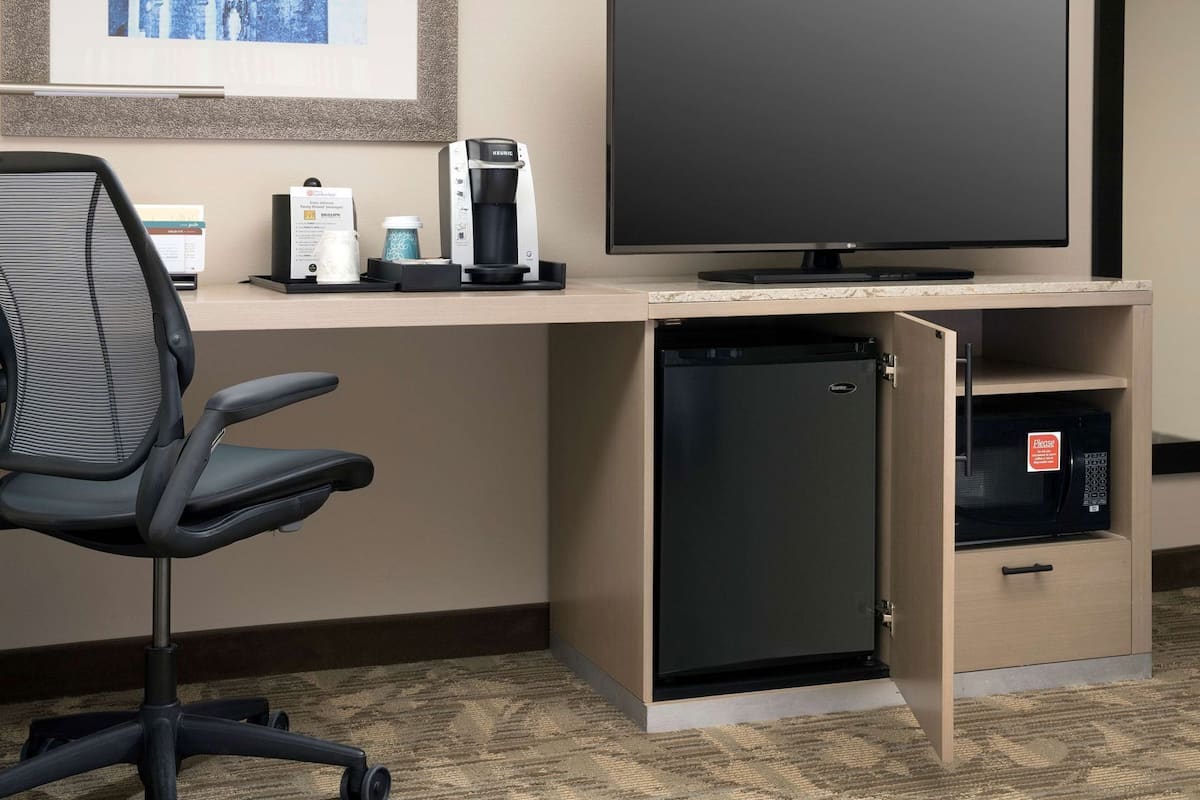 Habitación de hotel con escritorio, una silla de oficina negra, cafetera Keurig, televisor de pantalla plana, refrigerador pequeño y microondas.