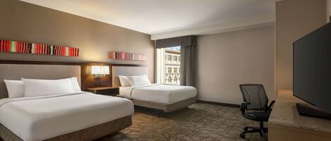 A hotel room with two beds, a desk, a chair, and a TV.