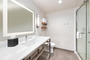 A modern bathroom with a large mirror, two sinks, a toilet, and a glass shower enclosure.