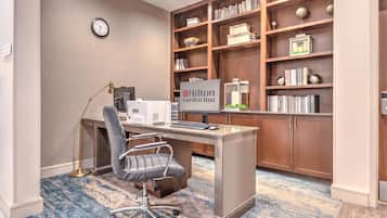 Een hotelkantoor met een bureau, stoel, computer en een boekenkast vol boeken en decoratieve objecten.