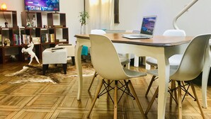 Ein modernes Wohnzimmer mit einem Holzesstisch, weißen Stühlen, einem Laptop, einem Fernseher auf einem Schrank und einem Bücherregal.
