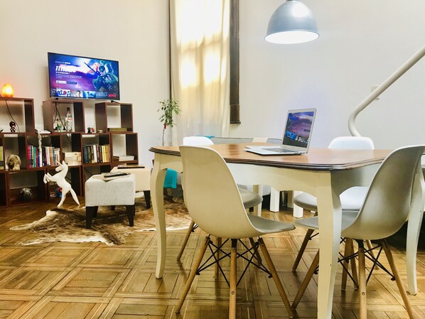 A modern living room with a wooden dining table, white chairs, a laptop, a TV on a stand, and a bookshelf. - La Casona del Alma (Buenos Aires)