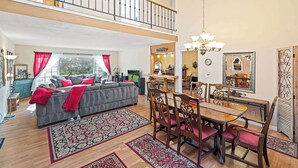 A spacious living room with a grey sofa, red cushions, and a dining area with wooden chairs and a glass table.