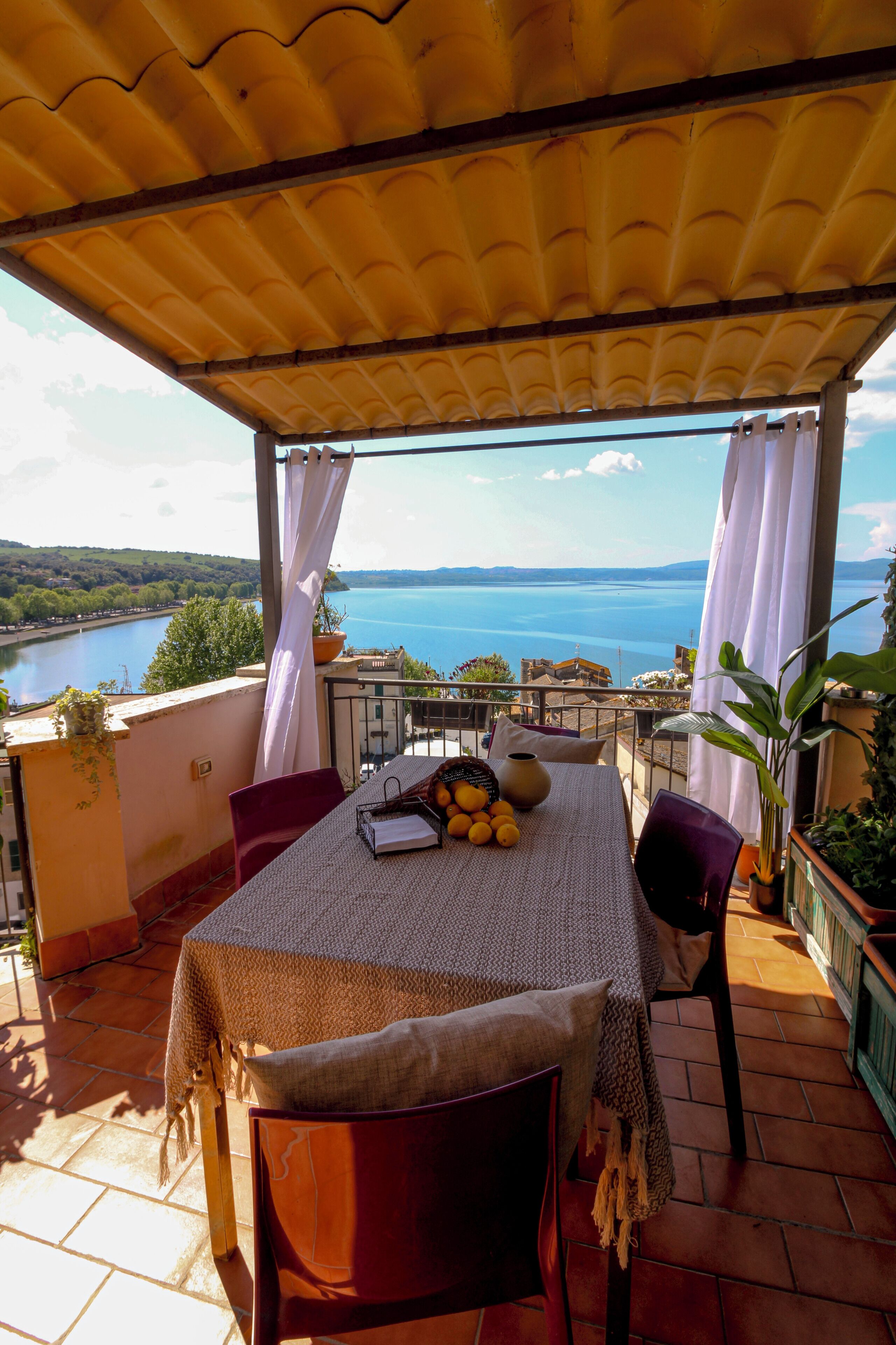 A terrace with a table set for two, overlooking a body of water and hills.