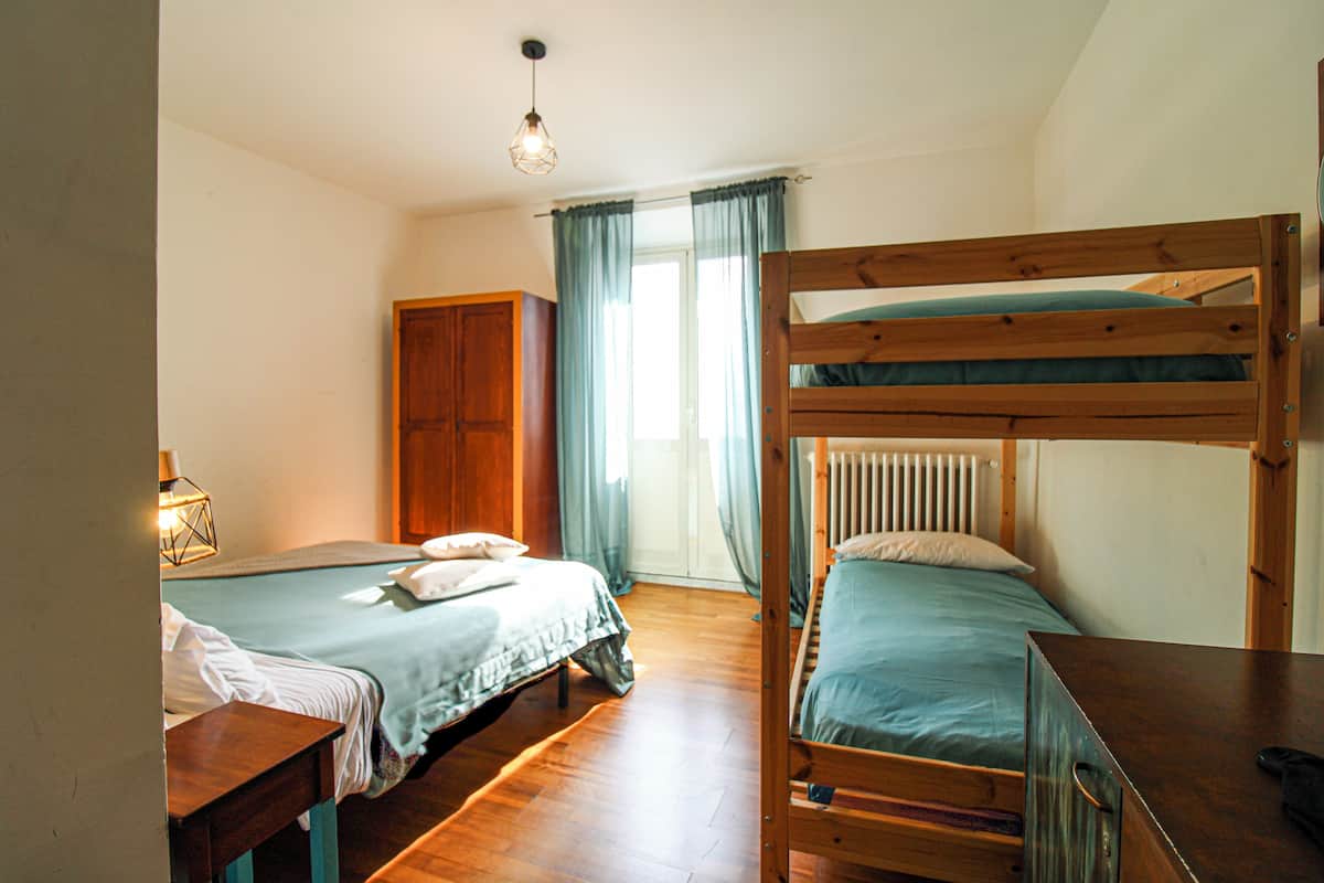 A room with two beds, a wooden wardrobe, a radiator, and a window with curtains.