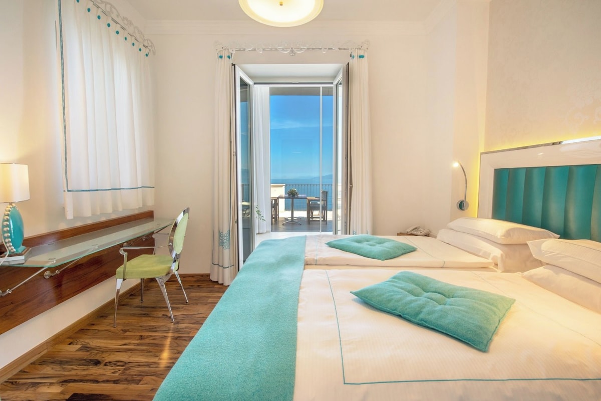 A hotel room with a balcony, a desk, a chair, and a bed with a headboard.