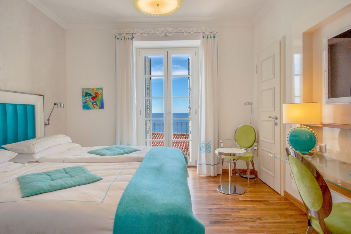A hotel room with two beds, a balcony with a view, a small table, and a chair.