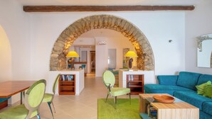 A living room with a stone archway, a blue sofa, green chairs, a wooden coffee table, and a bookshelf.