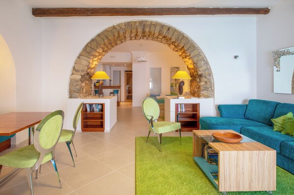 A living room with a stone archway, a blue sofa, green chairs, a wooden coffee table, and a bookshelf. - Piccolo Grand Hotel (Pizzo)