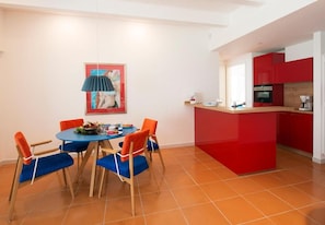 A dining area with a round table, four chairs, a pendant light, and a red kitchen island. - Piccolo Grand Hotel (Pizzo)