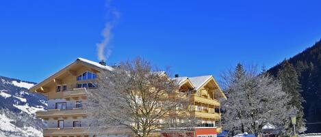 Un edificio de varios pisos con balcones, rodeado de árboles nevados y montañas.