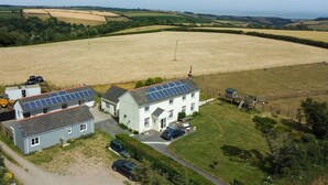 Ein ländliches Anwesen mit zwei Häusern, eines davon mit Solaranlage, umgeben von Feldern und einem kleinen Teich.