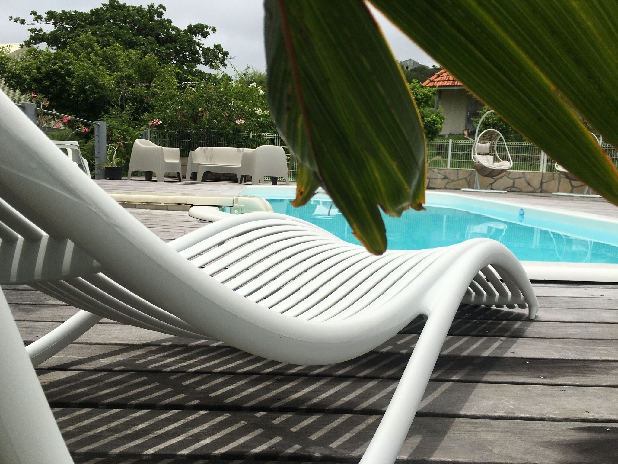 A poolside area with a white lounge chair, a pool, and a stone wall in the background.