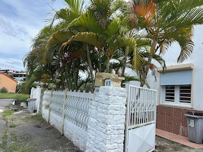 A gated residential area with a white stone wall, a numbered sign, and a building with a blue shuttered window.