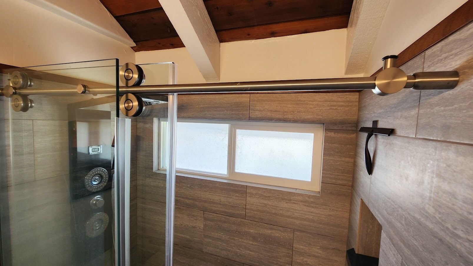 A shower area with a glass door, a wooden wall, and a window.