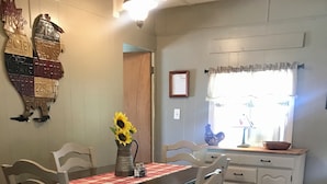 Un comedor con una mesa dispuesta para cuatro personas, rodeada de sillas de madera con cojines negros. Un jarrón con girasoles está sobre la mesa, y un certificado enmarcado cuelga de la pared.