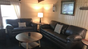 Una sala de estar acogedora con dos sofás de cuero negro, una mesa de centro de madera y una mesita auxiliar con una lámpara.