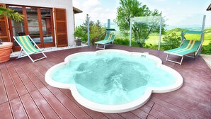 Un bain à remous sur une terrasse en bois, avec deux chaises longues, une plante en pot et une vue sur un paysage verdoyant.