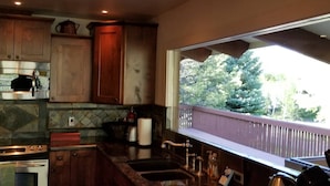 A kitchen with wooden cabinets, a stainless steel range hood, a large window with a view of trees, and a built-in oven. - The Perfect Sun Valley Vacation Home (Sun Valley)