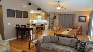 A spacious living area with a wooden dining table, a gray sofa, and a kitchen in the background. - Lakefront Oasis: Dock, Hot Tub, Views, Nearby Rafting, Zipline, and More! (Almond)