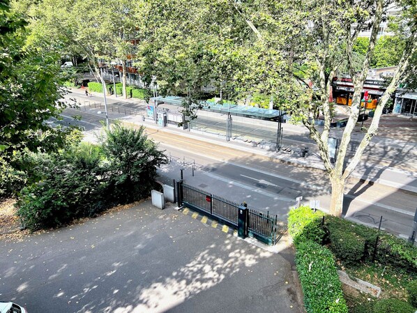 Une vue d’une rue avec une entrée fermée par un portail, des arbres et un arrêt de bus.