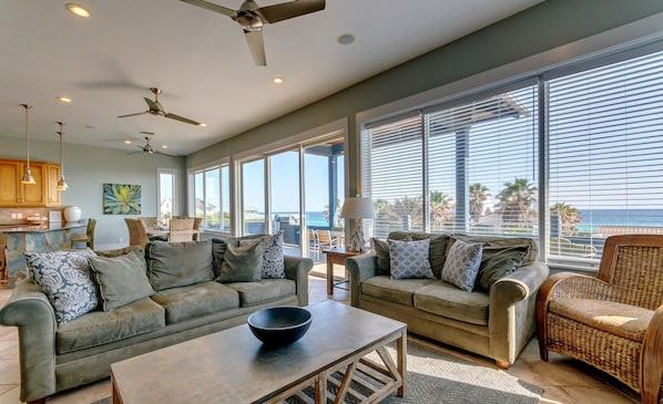 A spacious living room with a large window offering a view of the ocean, a ceiling fan, and a dining area with a view.