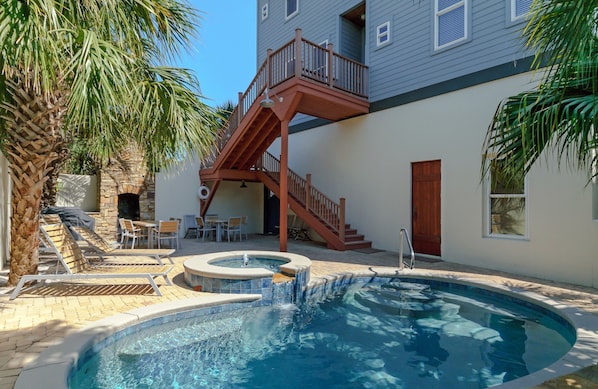 A swimming pool with a wooden deck, lounge chairs, and a stone wall.