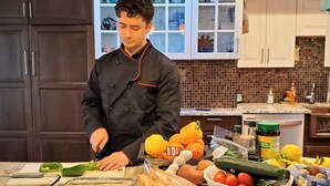 Un chef preparando comida en una cocina con alacenas, una encimera y diversos alimentos.