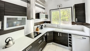 A modern kitchen with dark cabinetry, a stainless steel refrigerator, a microwave, and a window with a view of greenery. - 4 Bedroom 3 Bathroom  Villa in Orient Bay, 5 min Walk to Beach and French bakery (Orient Bay)