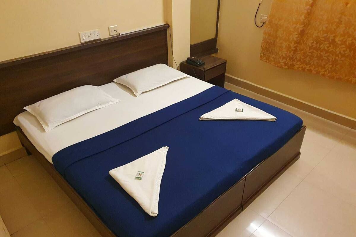 A neatly made bed with a blue bedspread and white pillows, a wooden headboard, and a small bedside table with a lamp.
