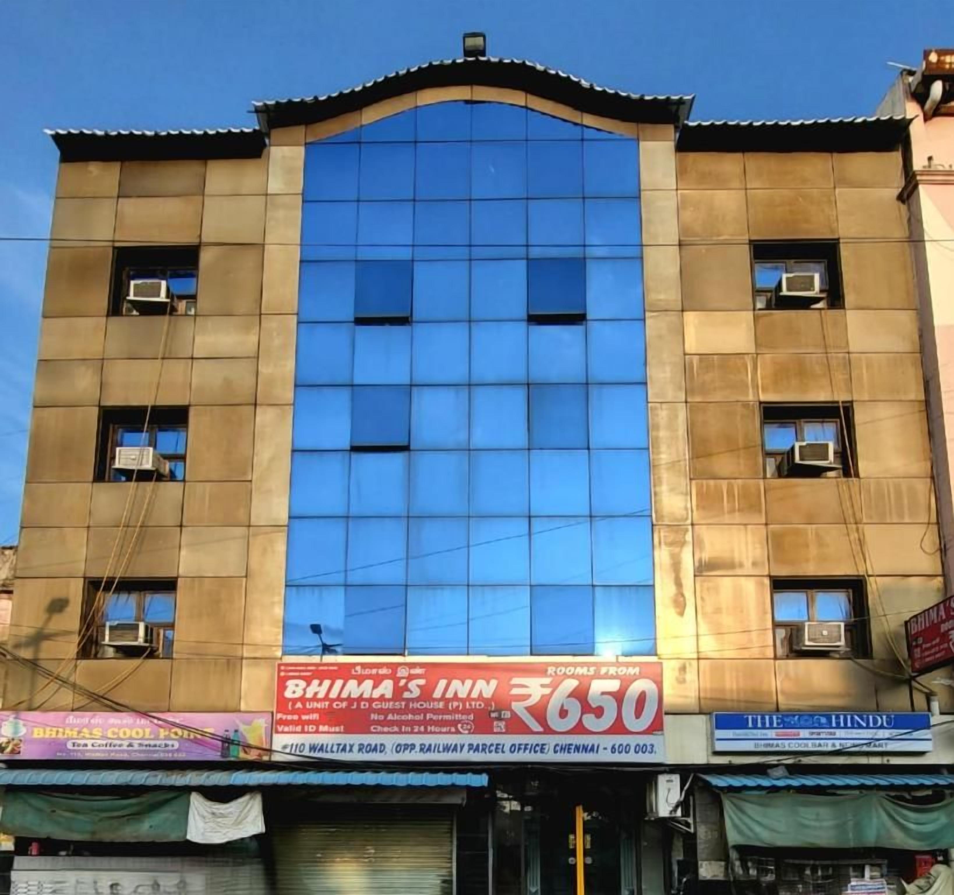 A building with a large glass facade, a sign for 'BHIMA'S INN' with room rates, and multiple air conditioning units.