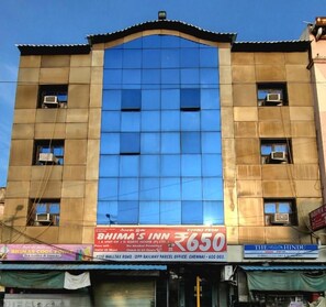 A building with a large glass facade, a sign for 'BHIMA'S INN' with room rates, and multiple air conditioning units.