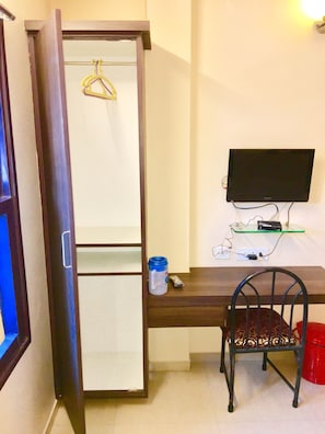 A room with a wardrobe, a desk with a computer, a chair, and a red trash bin.