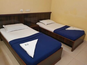 Two single beds with wooden headboards, white linens, and blue bedspreads in a hotel room.