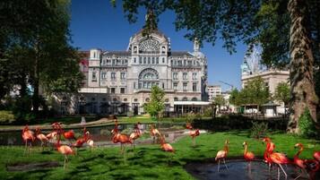 A large historic building with a central dome and arched windows, surrounded by a well-maintained garden with flamingos.