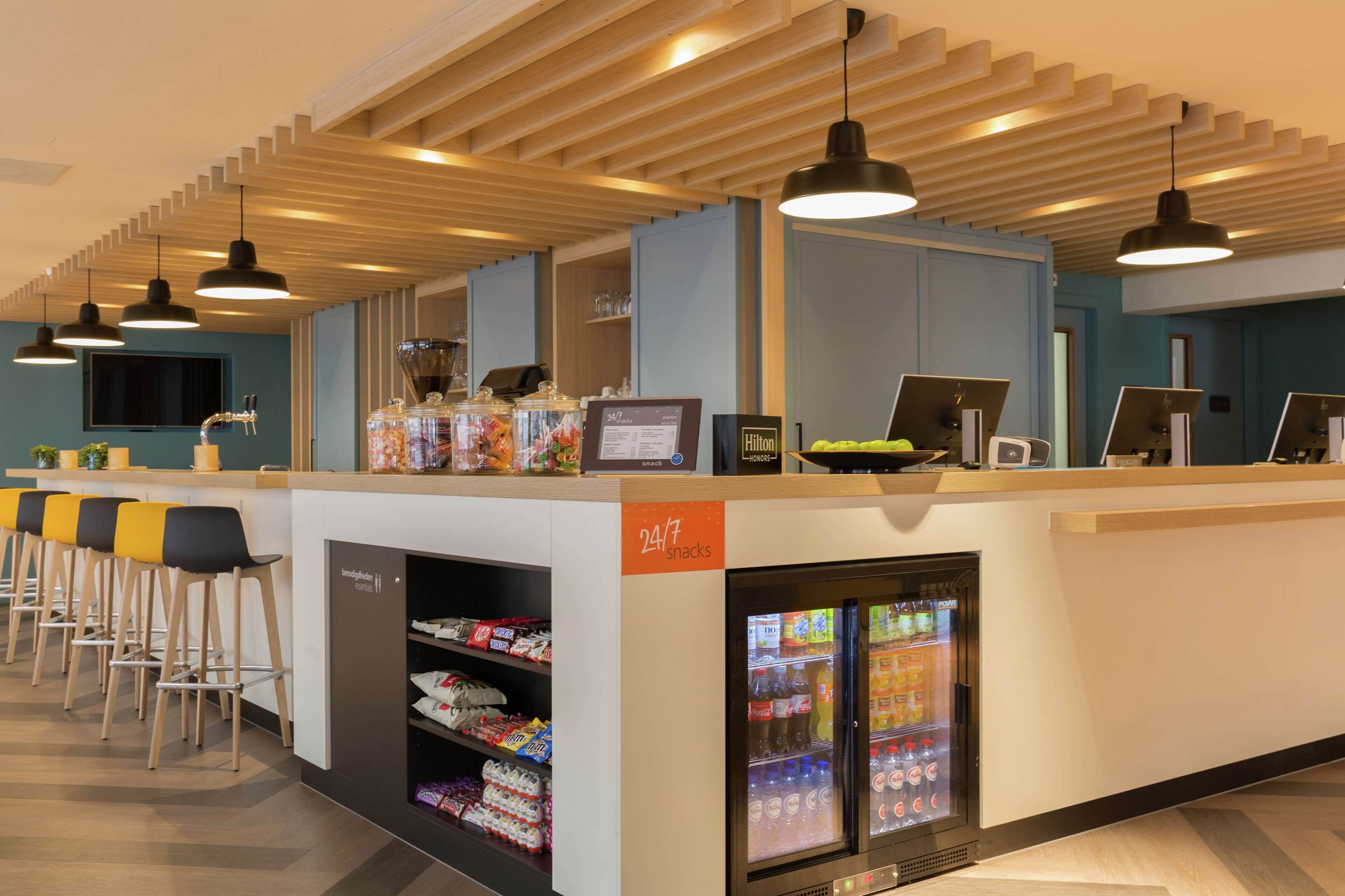 A 24/7 snack bar with a refrigerated display, bar stools, and a digital menu board.