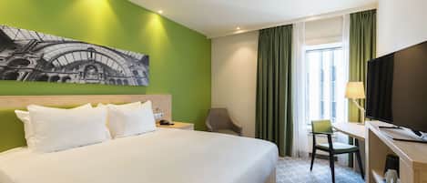 A hotel room with a large bed, a desk with a chair, a television, and a window with curtains.