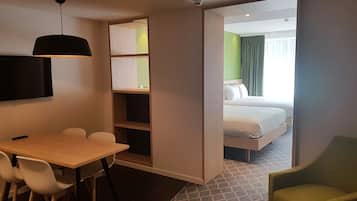 Una habitación de hotel con cama, escritorio, sillas, televisión y estantería.