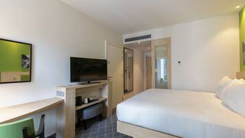 A hotel room with a bed, a desk with a television, a chair, and a small seating area.