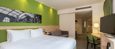 A hotel room with a large bed, a desk with a chair, a television, and a painting on the wall.