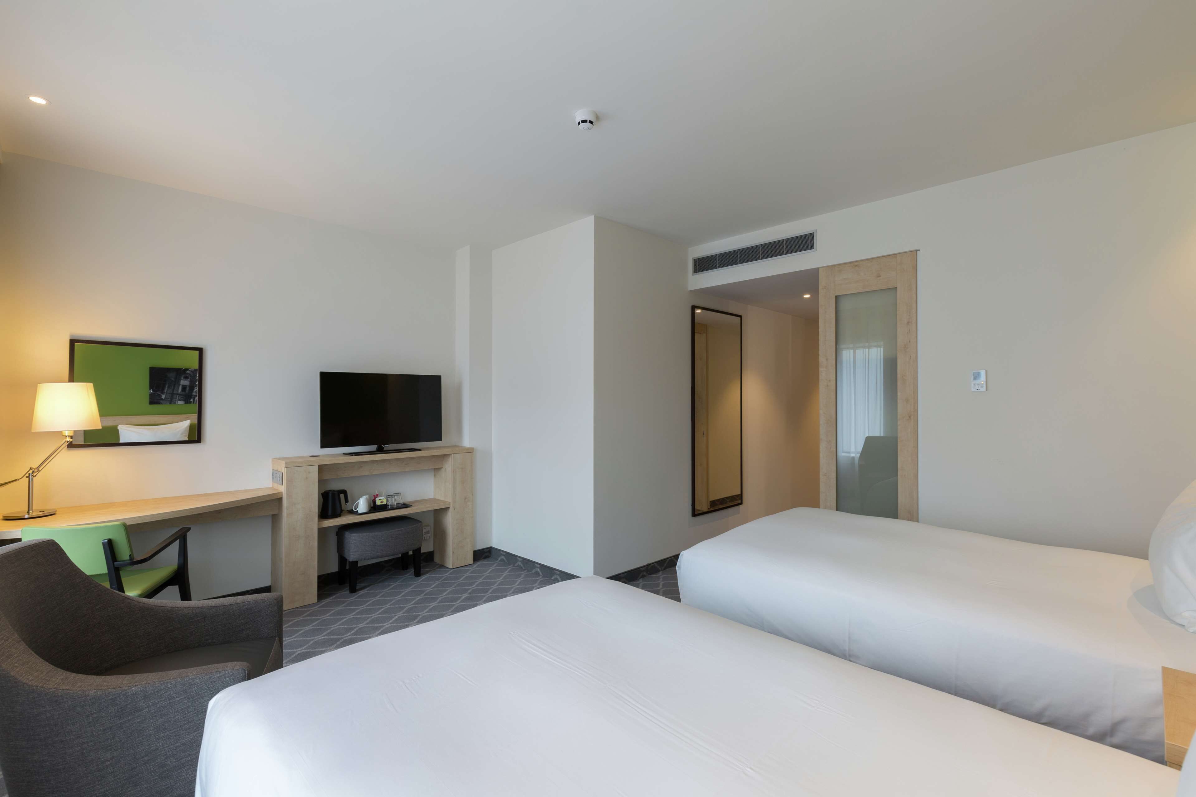 A hotel room with two beds, a desk with a television, a chair, and a lamp.