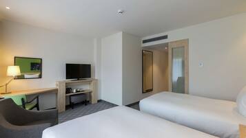 Una habitación de hotel con dos camas, un escritorio, un televisor, una silla y una lámpara.