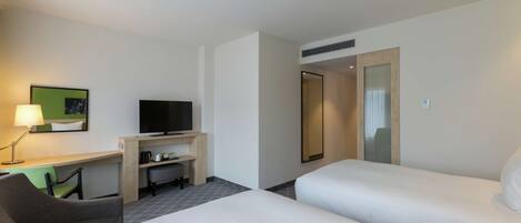 A hotel room with two beds, a desk with a television, a chair, and a lamp.