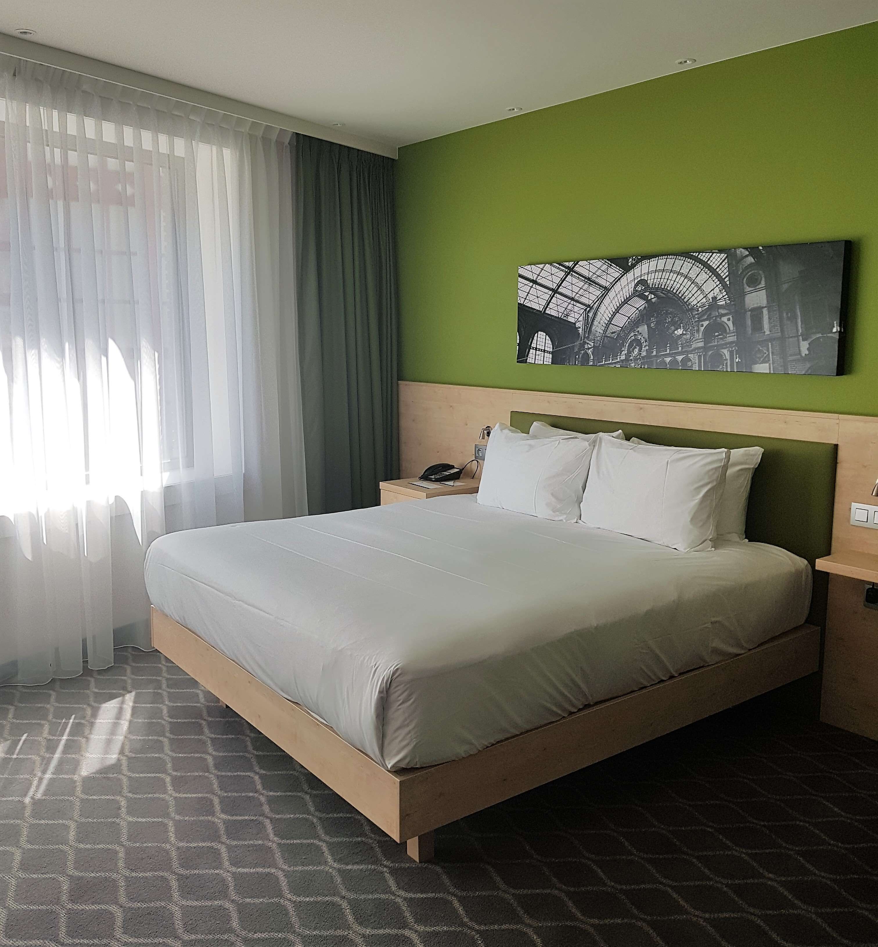 Une chambre d’hôtel avec un grand lit, un mur vert, une œuvre d’art en noir et blanc et un sol à motifs.