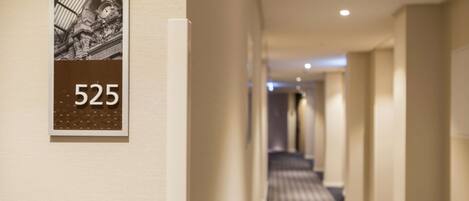 A hotel hallway with a number sign '525' on the wall, a patterned carpet, and a modern ceiling with recessed lighting.