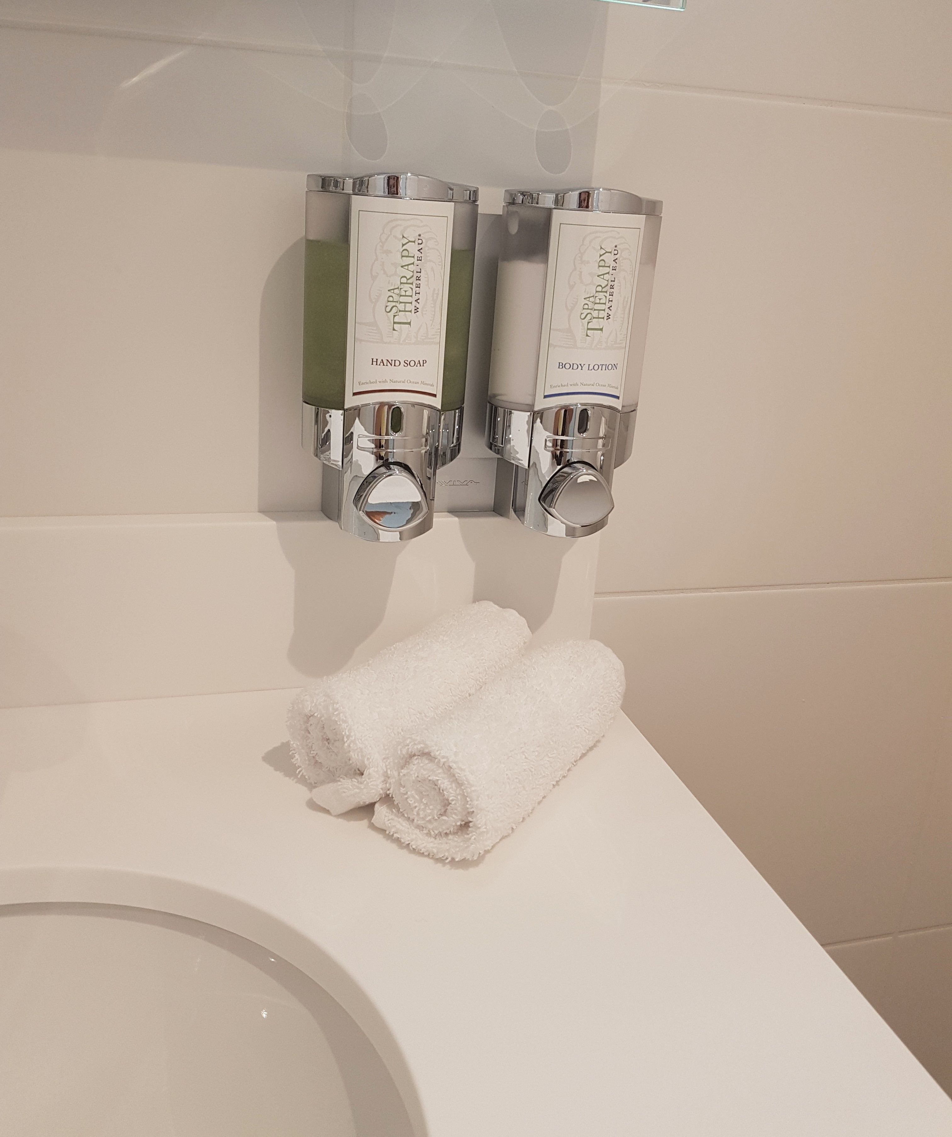 Un baño con un lavamanos blanco, dos dispensadores de jabón para manos y dos dispensadores de crema corporal.