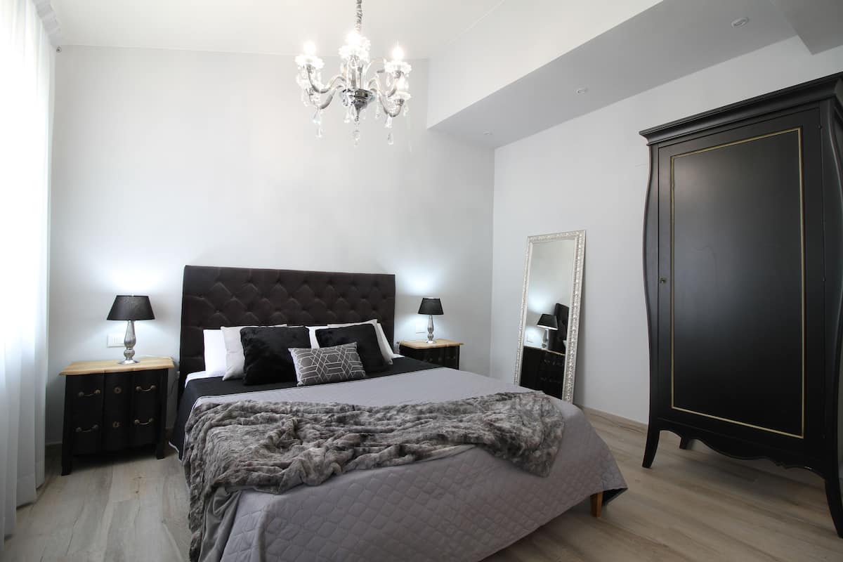 A bedroom with a large bed, a dark wooden wardrobe, a chandelier, and bedside lamps.